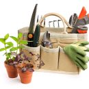 A gardening equipment tool bag next to potted plants of mint and basil herb spring seedlings. The flower pot containers, work gloves, pruning shears, sprinkler, and other objects are ready for planting and preparing springtime backyard hobby gardens. Sill life, cut out and isolated on white background with no people.